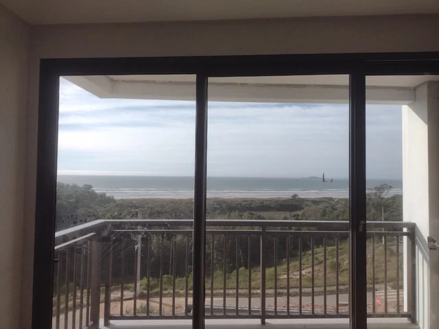 Vista interna de uma esquadria de correr com vidro e sacada com guarda-corpo metálico.