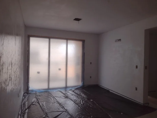 Ambiente interno de paredes claras, esquadria coberta e película de proteção sobre o piso.