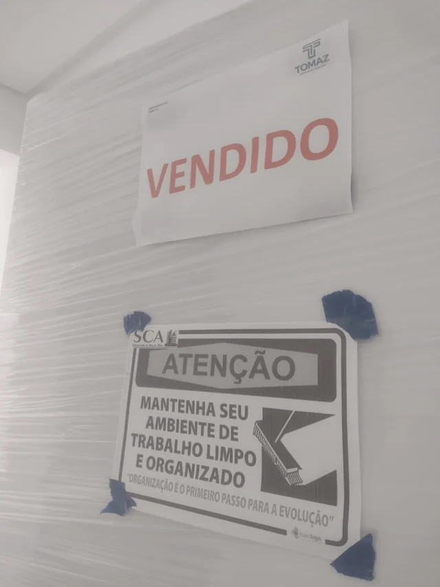 Porta protegida com película e avisos escritos de vendido e de organização do ambiente de trabalho.