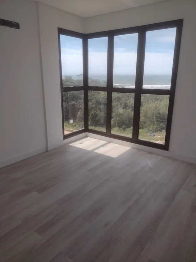 Ambiente interno com piso de padrão amadeirado e esquadria escura envidraçada de canto.